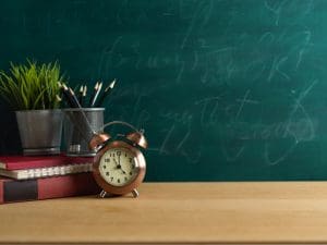 Study table with clock, stationery, plant pot and copy space on wooden table with chalkboard wall background
